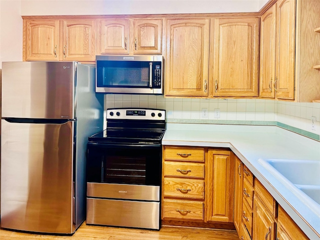 kitchen with tasteful backsplash, stainless steel appliances, sink, and light hardwood / wood-style floors