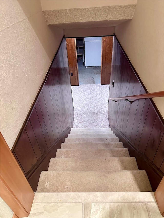 staircase featuring carpet flooring and wood walls