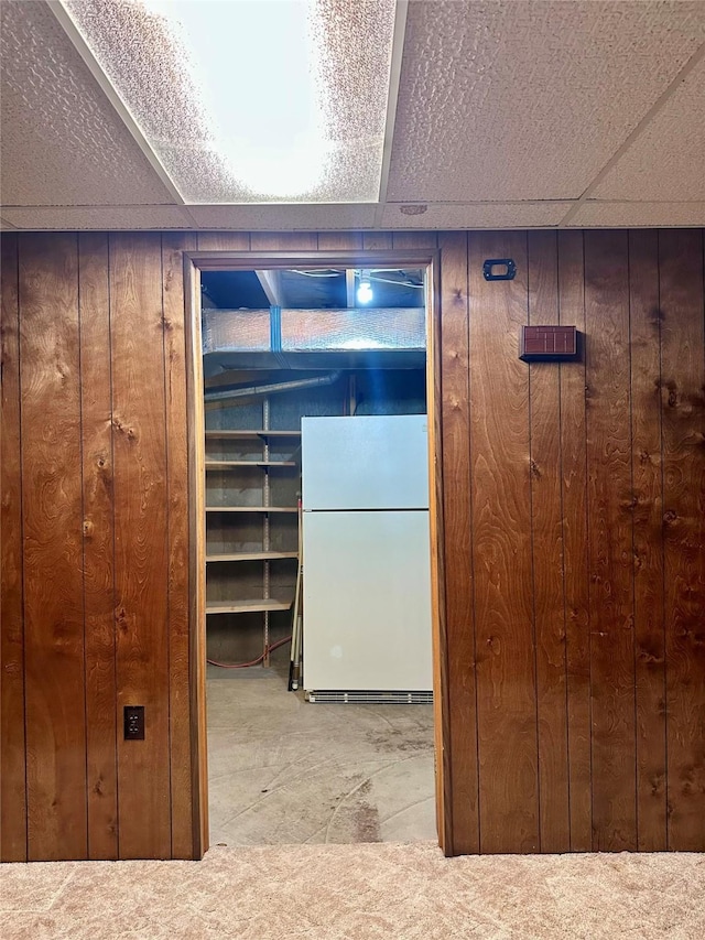 interior space featuring white refrigerator, wooden walls, light carpet, and a drop ceiling