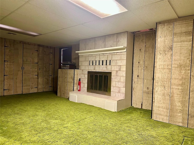 basement with wooden walls, a large fireplace, and carpet flooring