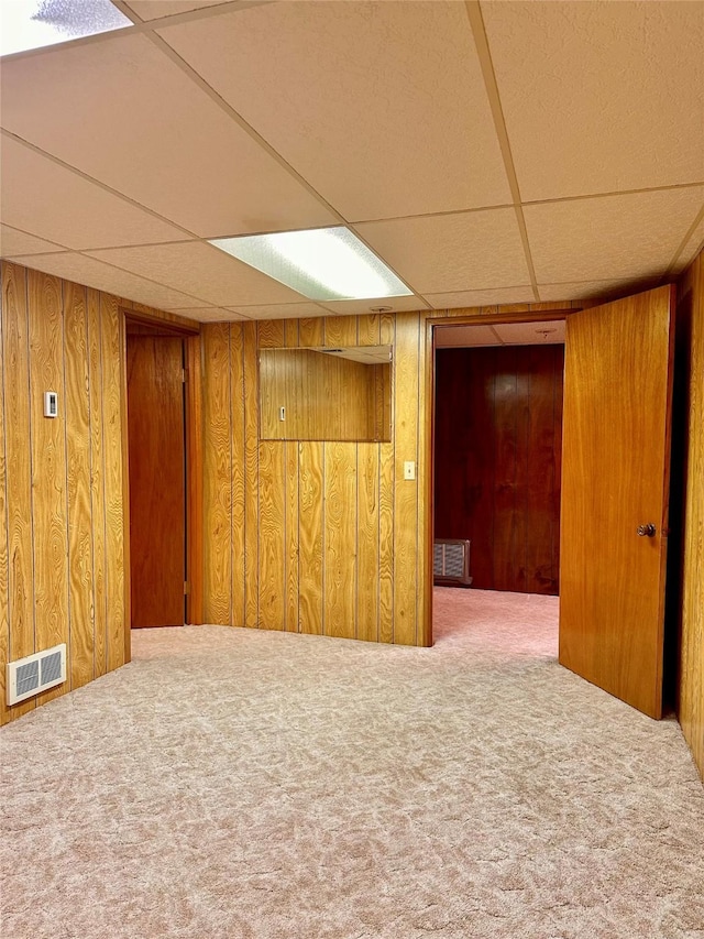 basement with a paneled ceiling, carpet flooring, and wood walls