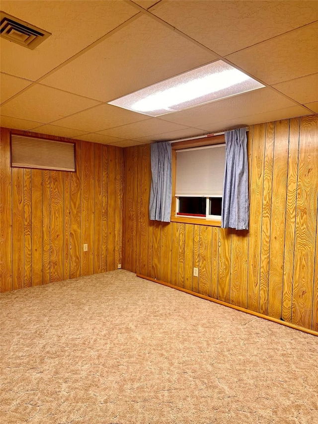 carpeted empty room featuring wooden walls and a paneled ceiling