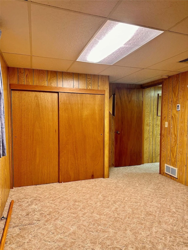 basement featuring wooden walls, carpet, and a drop ceiling