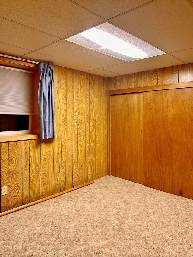 basement featuring carpet floors, wooden walls, and a paneled ceiling