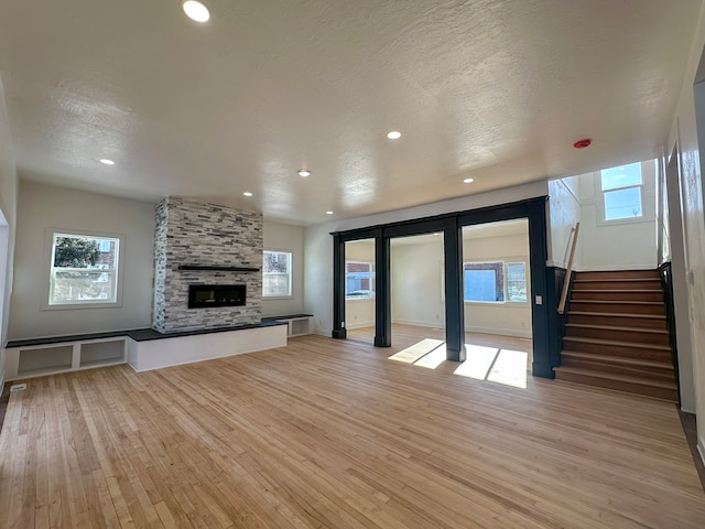 unfurnished living room with a stone fireplace, a textured ceiling, and light wood-type flooring