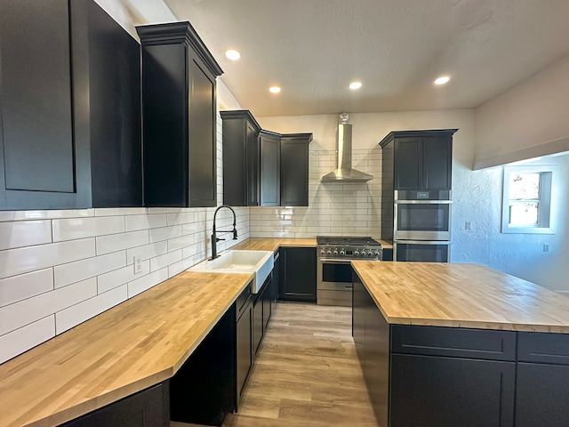 kitchen featuring wood counters, wall chimney exhaust hood, appliances with stainless steel finishes, and sink