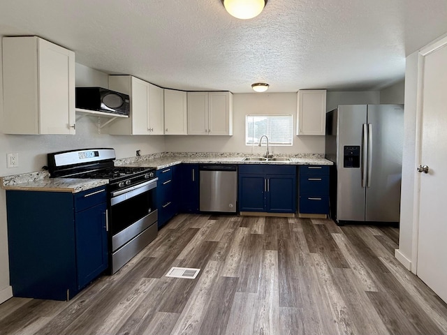 kitchen with appliances with stainless steel finishes, blue cabinets, sink, and white cabinets