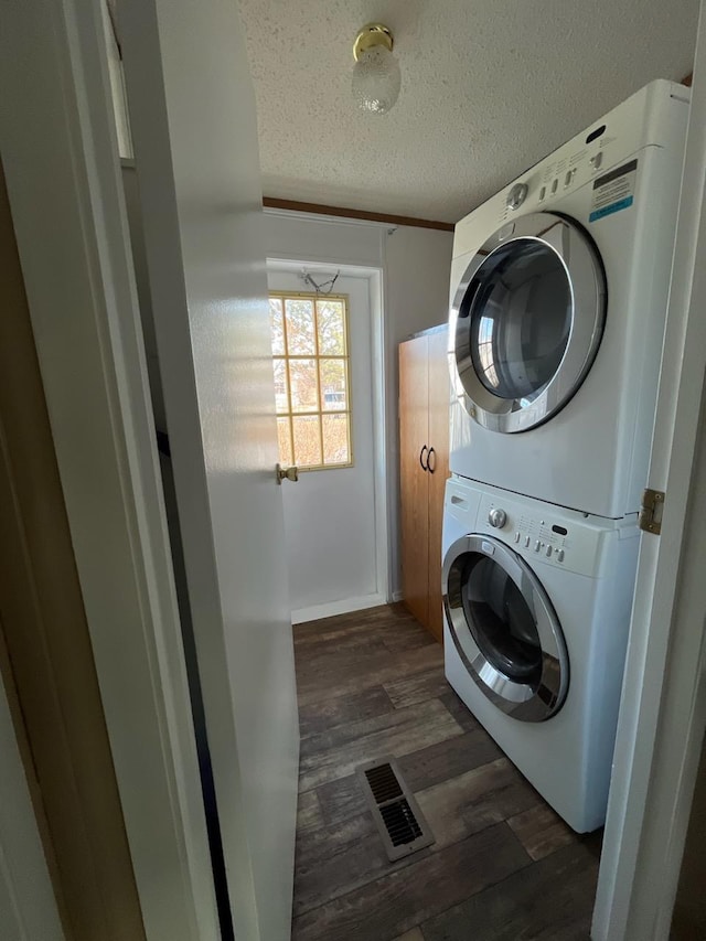 clothes washing area featuring dark wood-type flooring, a textured ceiling, and stacked washing maching and dryer