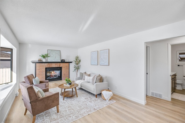 living room featuring a textured ceiling, a fireplace, a healthy amount of sunlight, and light wood-type flooring