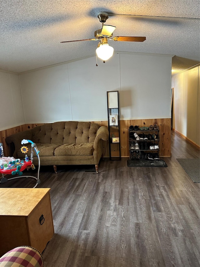 living room featuring ceiling fan, a textured ceiling, dark hardwood / wood-style flooring, vaulted ceiling, and wood walls