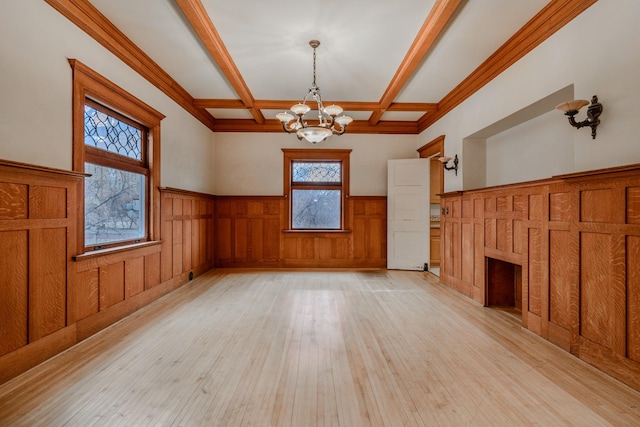 unfurnished living room featuring beam ceiling, wooden walls, coffered ceiling, a notable chandelier, and light hardwood / wood-style floors