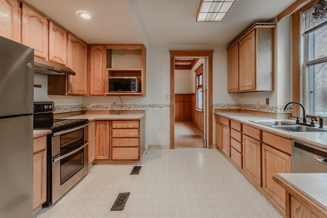 kitchen with wood walls, appliances with stainless steel finishes, sink, and light brown cabinets