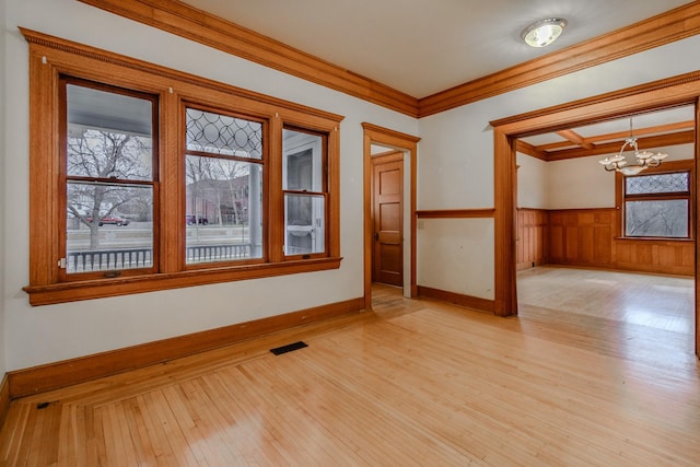 empty room with ornamental molding, a chandelier, and light hardwood / wood-style floors