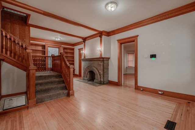 living room with a brick fireplace, ornamental molding, built in features, and light hardwood / wood-style floors