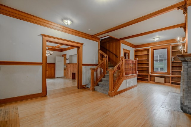 unfurnished living room featuring crown molding, an inviting chandelier, light wood-type flooring, and built in shelves