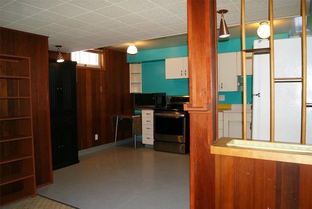 kitchen featuring stainless steel electric stove, white refrigerator, white cabinets, and wood walls