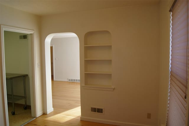 empty room with built in features and light hardwood / wood-style flooring