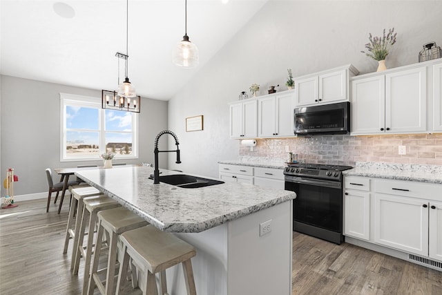 kitchen with sink, stainless steel gas stove, white cabinetry, decorative light fixtures, and an island with sink