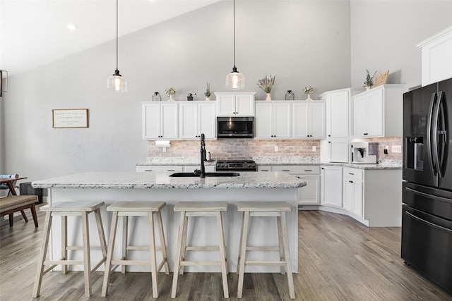 kitchen featuring decorative light fixtures, black refrigerator with ice dispenser, an island with sink, and white cabinets