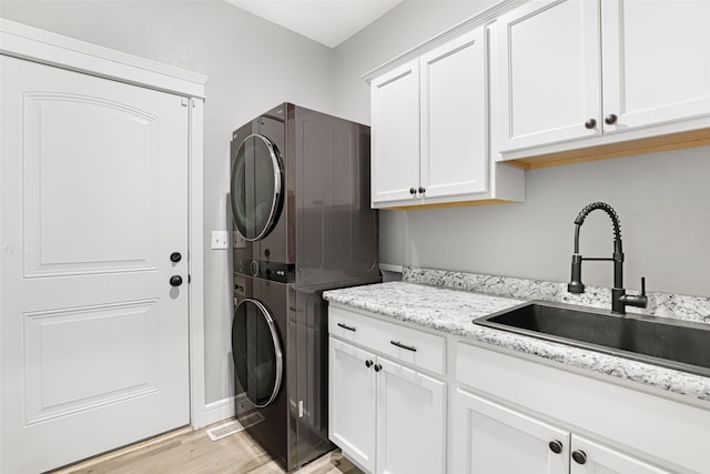 laundry room with cabinets, stacked washing maching and dryer, sink, and light wood-type flooring