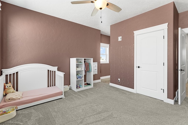 bedroom with ceiling fan, a nursery area, a textured ceiling, and carpet flooring