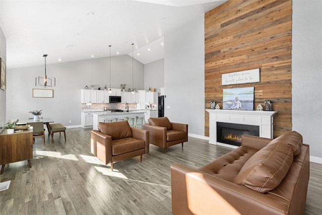 living room with wood walls, high vaulted ceiling, and light hardwood / wood-style flooring