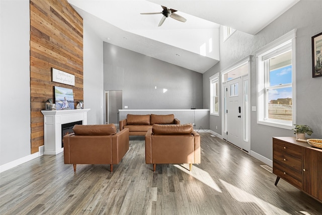 living room with ceiling fan, high vaulted ceiling, wooden walls, and hardwood / wood-style floors