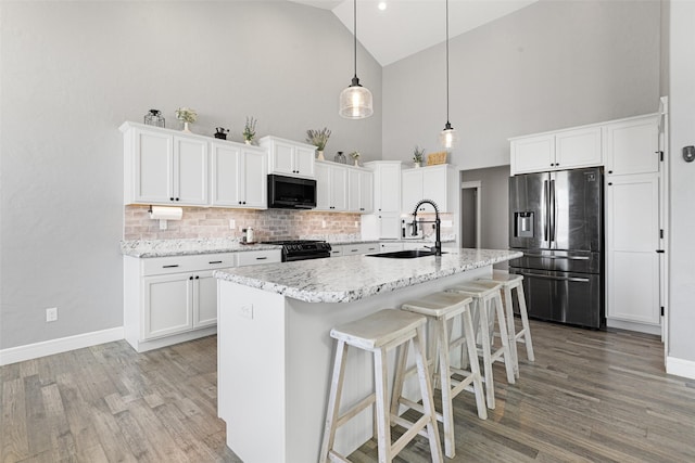 kitchen with sink, hanging light fixtures, stainless steel fridge, a kitchen island with sink, and white cabinets