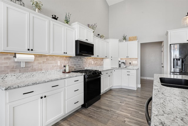 kitchen featuring stainless steel fridge with ice dispenser, white cabinets, light stone counters, and black gas range