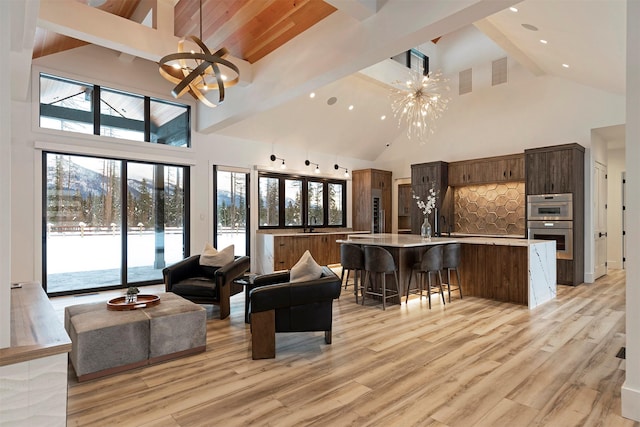 living room featuring high vaulted ceiling, beam ceiling, light wood-type flooring, and a notable chandelier