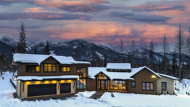 snow covered back of property featuring a garage and a mountain view