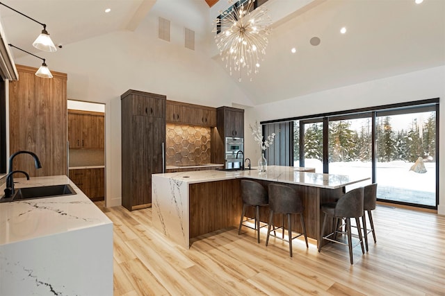 kitchen featuring a spacious island, sink, light stone counters, decorative light fixtures, and a notable chandelier