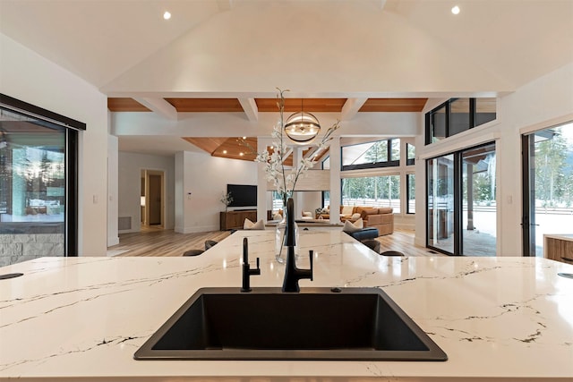 kitchen featuring beamed ceiling, sink, light hardwood / wood-style floors, light stone countertops, and an inviting chandelier