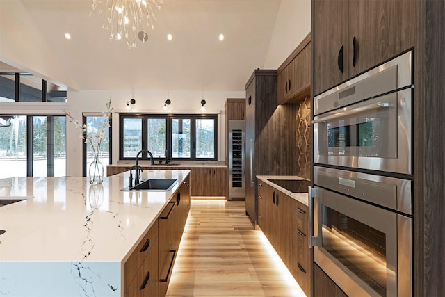 kitchen featuring a large island, sink, light stone counters, stainless steel double oven, and light wood-type flooring