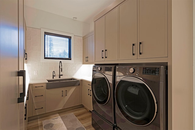 laundry area featuring light hardwood / wood-style floors, sink, washing machine and dryer, and cabinets