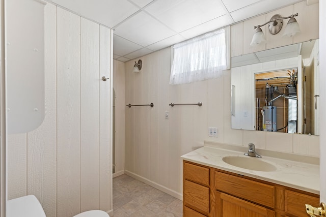 bathroom with gas water heater, a drop ceiling, vanity, and toilet