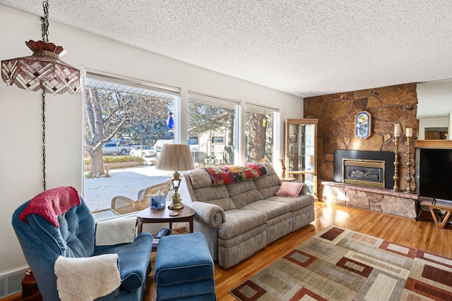 living room with hardwood / wood-style flooring, a stone fireplace, and a textured ceiling