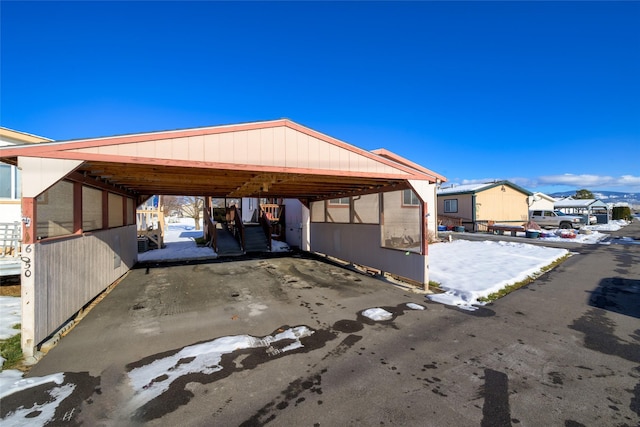 snow covered parking area featuring a carport