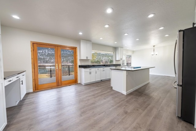 kitchen with pendant lighting, white cabinets, stainless steel fridge, a center island, and light hardwood / wood-style flooring