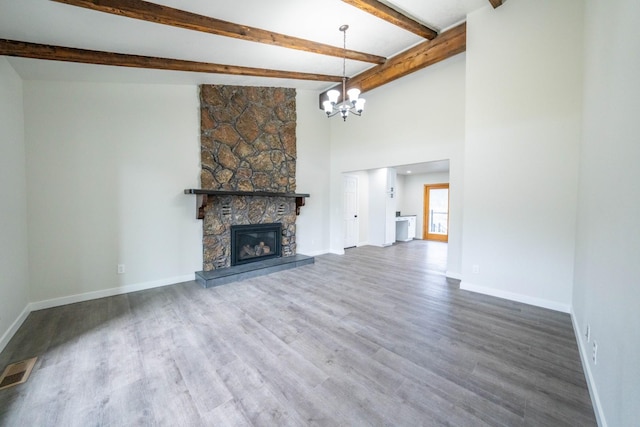 unfurnished living room with beam ceiling, a notable chandelier, hardwood / wood-style flooring, a towering ceiling, and a fireplace