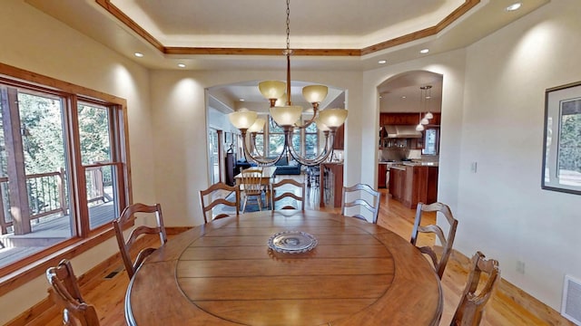 dining area featuring a notable chandelier, light hardwood / wood-style flooring, and a raised ceiling