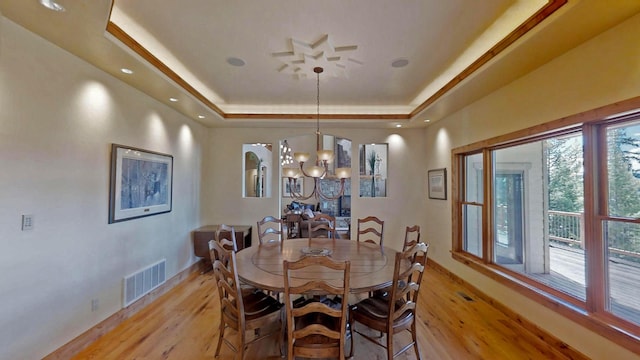 dining area featuring a raised ceiling, an inviting chandelier, and light wood-type flooring