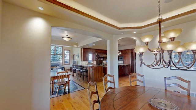 dining space featuring a chandelier, a raised ceiling, and light wood-type flooring