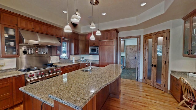 kitchen featuring extractor fan, appliances with stainless steel finishes, an island with sink, hanging light fixtures, and a tray ceiling