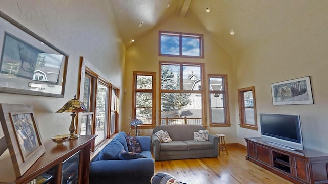 living room with beam ceiling, light hardwood / wood-style flooring, high vaulted ceiling, and plenty of natural light