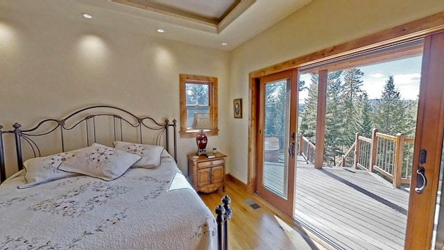 bedroom featuring a raised ceiling, light hardwood / wood-style flooring, access to exterior, and french doors