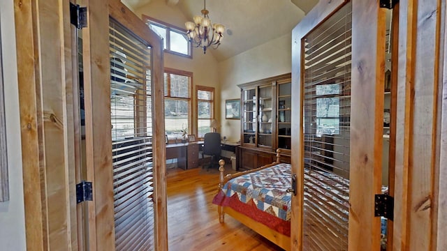 bedroom featuring a notable chandelier, built in desk, wood-type flooring, and high vaulted ceiling