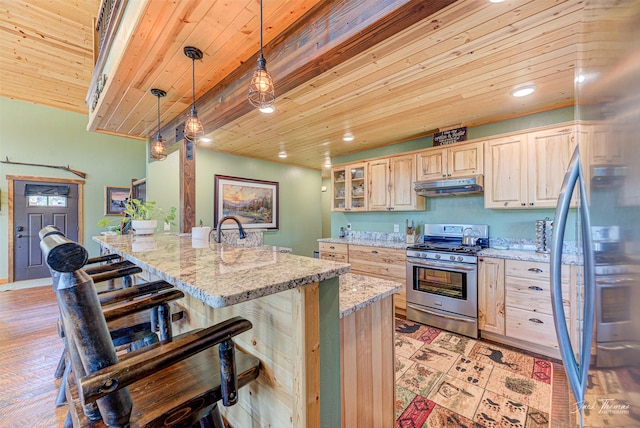 kitchen featuring decorative light fixtures, a kitchen breakfast bar, stainless steel gas range oven, light stone countertops, and a center island with sink