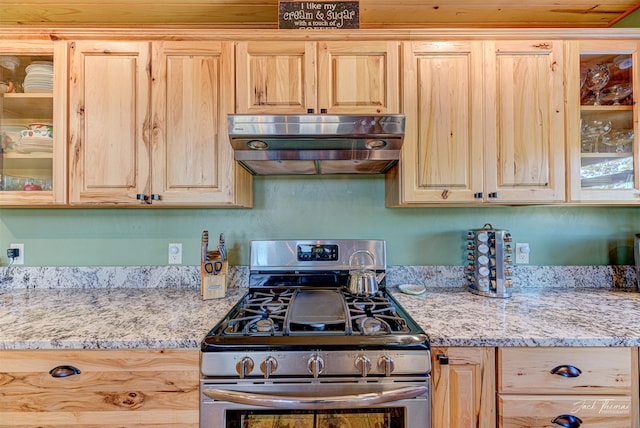 kitchen with stainless steel gas range oven, light stone counters, and light brown cabinetry