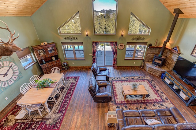 living room with dark hardwood / wood-style flooring, high vaulted ceiling, a wood stove, and wood ceiling